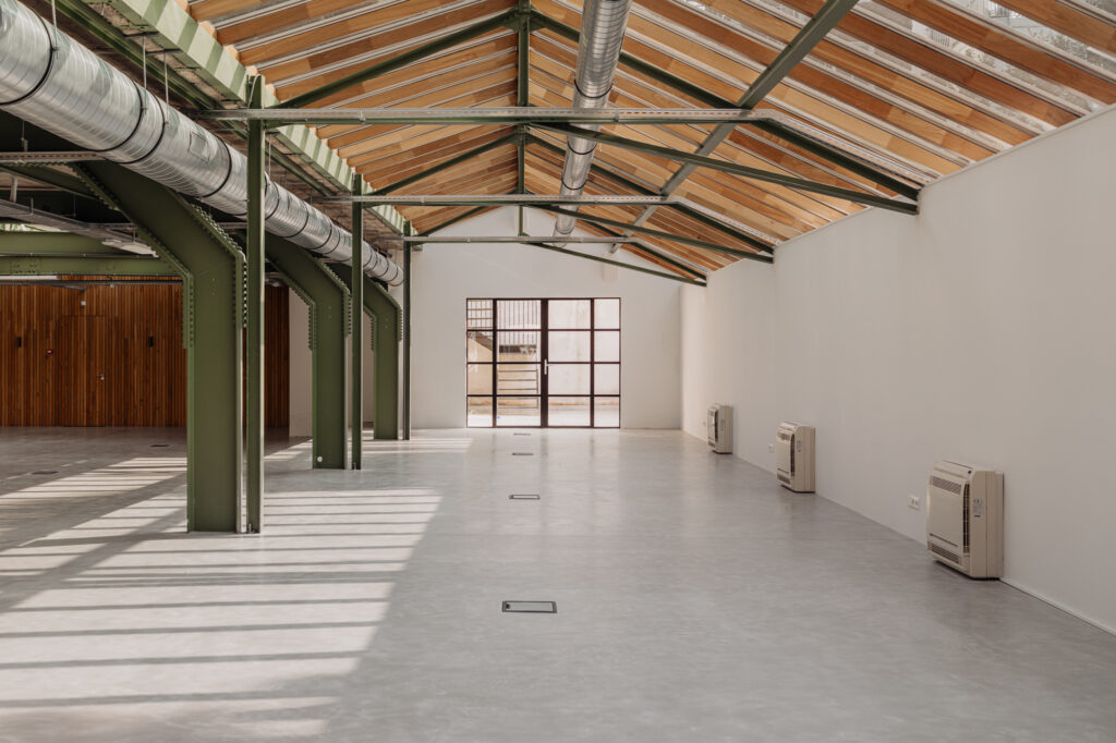 Licht en open industrieel interieur aan de Plantage Middenlaan met groene stalen balken, glazen dak en betonnen vloer.